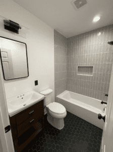 Modern bathroom remodel featuring gray vertical tile shower, built-in niche, black hexagon tile flooring, and contemporary vanity.
