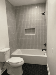 Modern bathroom remodel featuring gray vertical tile shower, built-in niche, black hexagon tile flooring, and contemporary vanity.