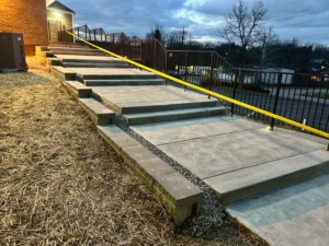 Progress photo of newly installed 50-foot-long, 9-foot-wide concrete steps with swirl hand-float finish, Allen Block retaining wall, and temporary safety railing in Mt. Healthy, Ohio.